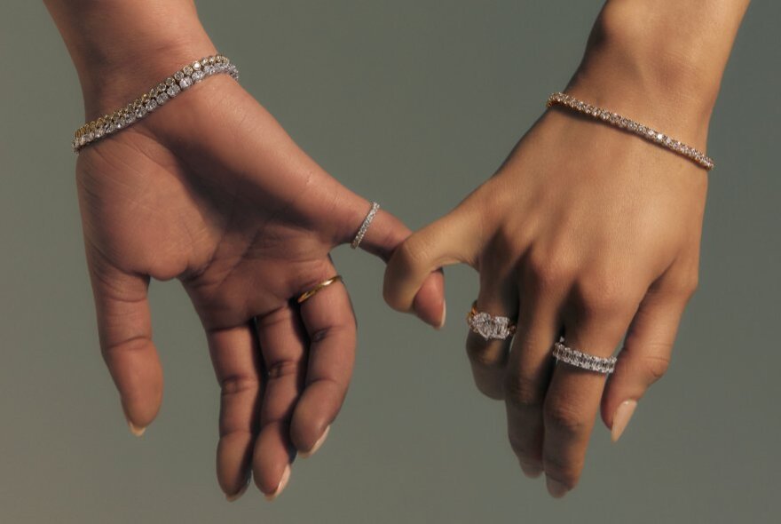Two hands wearing rings and bracelets, with little fingers linked.