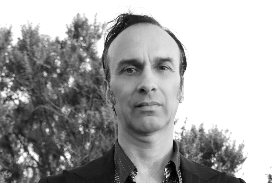 Head and shoulders of Melbourne composer and guitarist Cam Butler, standing outside; black and white.