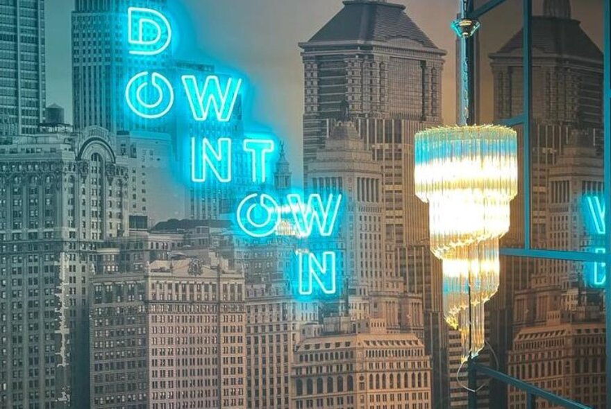 Chandelier and neon signage against wallpaper of city buildings.