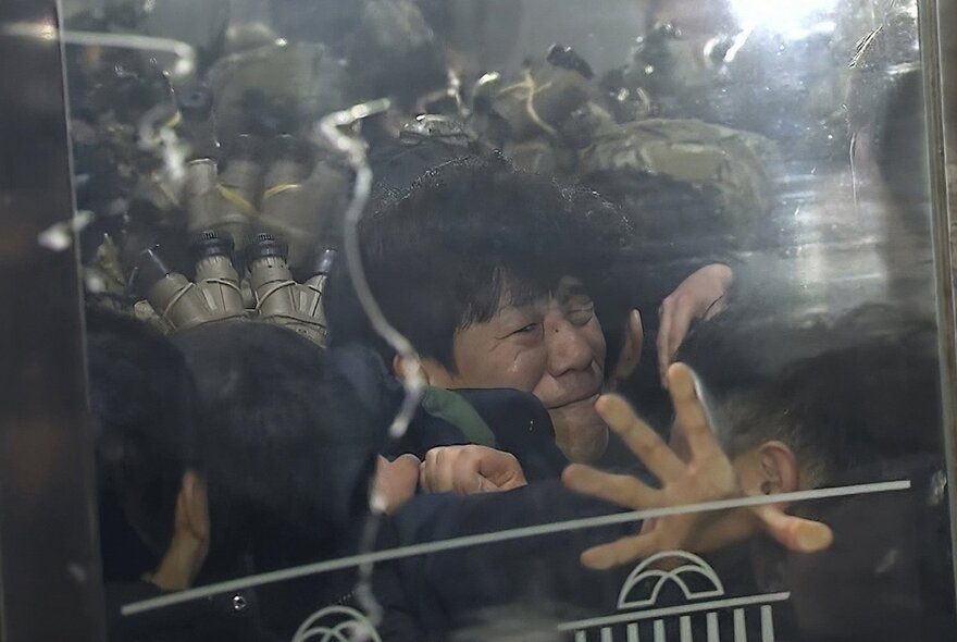 A still from the 2026 political documentary The Seoul Guardians, shows a person with their face pressed up against a plastic shield or door.