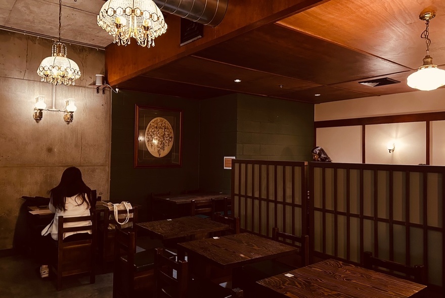 Warm wooden interior of Omo cafe with hanging lights and several dining tables and chairs.