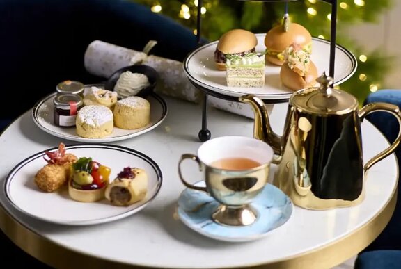 A small table with delicate desserts, a high tea stand and a golden teacup and teapot.