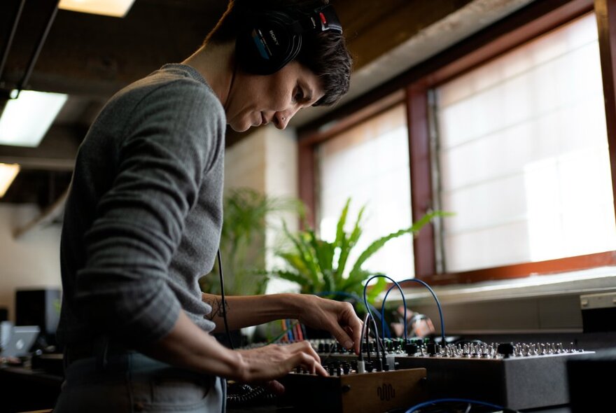 Person wearing headphones standing at a mixing desk.