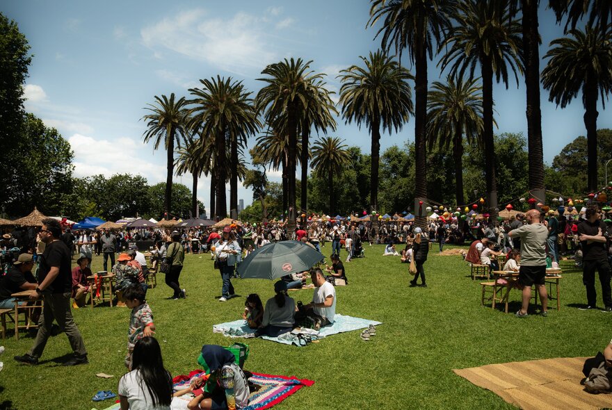 People on picnic blankets in the gardens with large palm trees. 