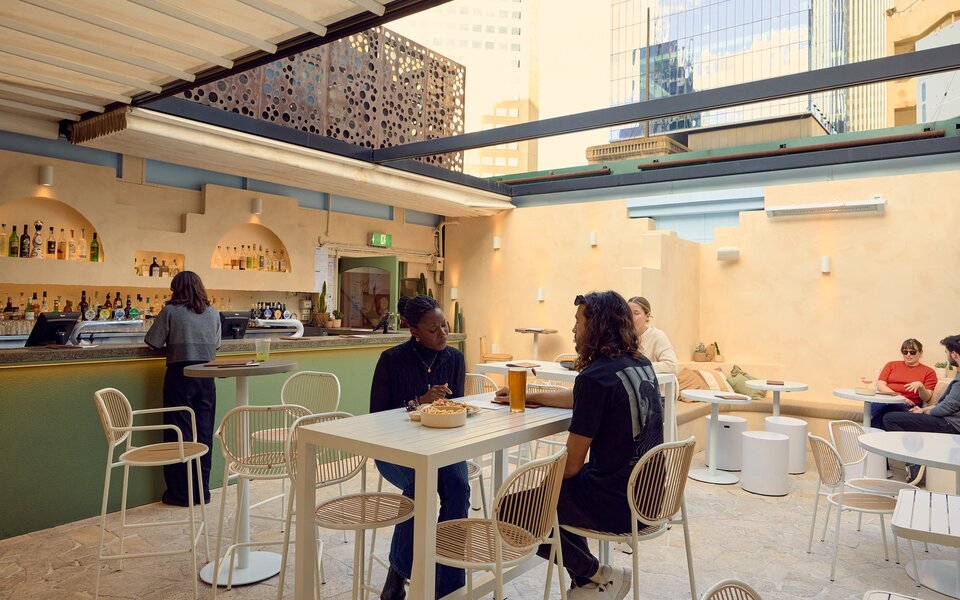 A partially covered rooftop bar with people drinking and eating inside.