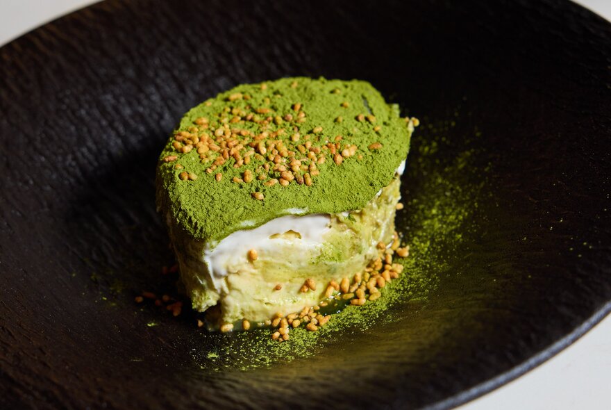 A green-coloured genmaicha tiramisu on a black plate.