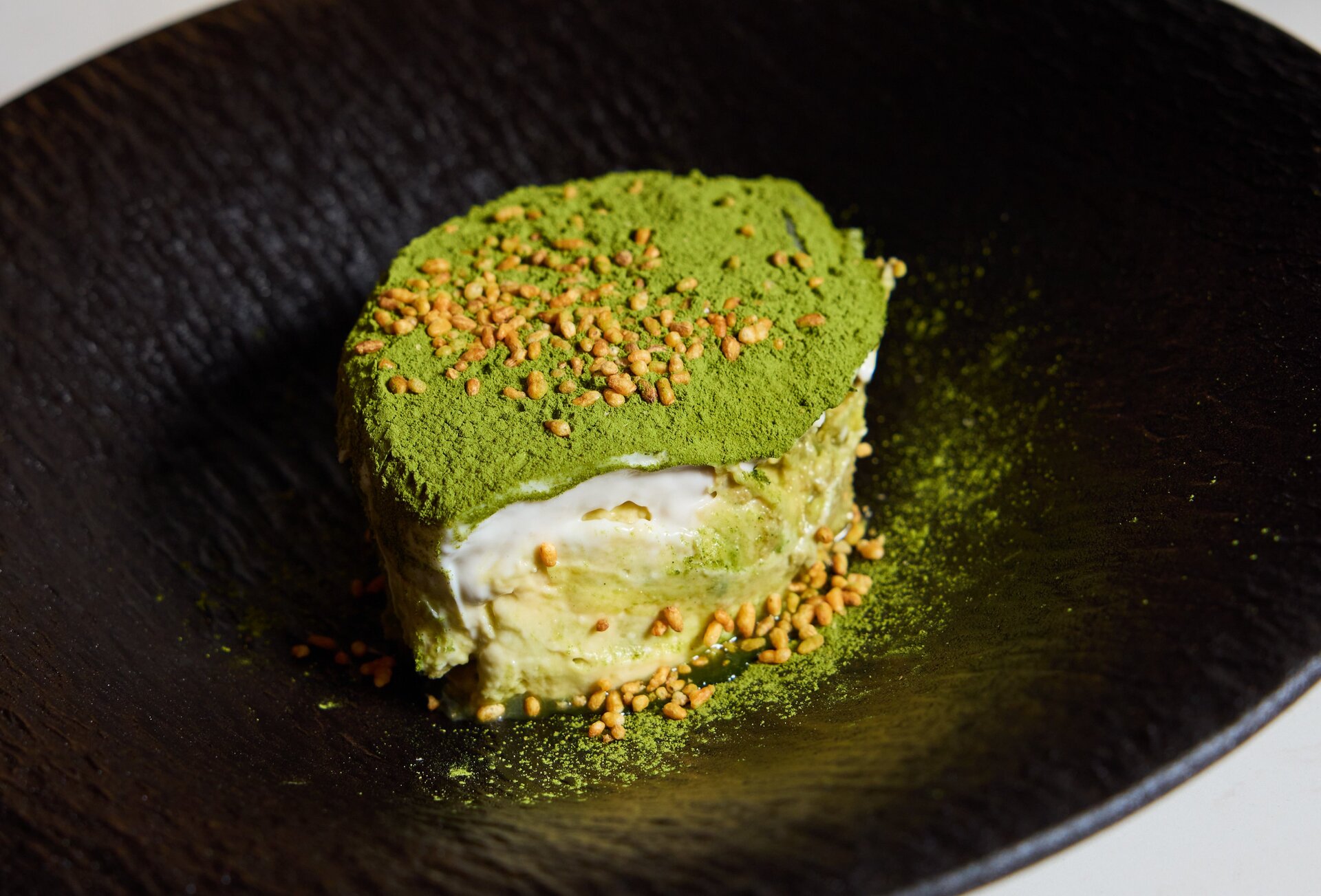 A green-coloured genmaicha tiramisu on a black plate.