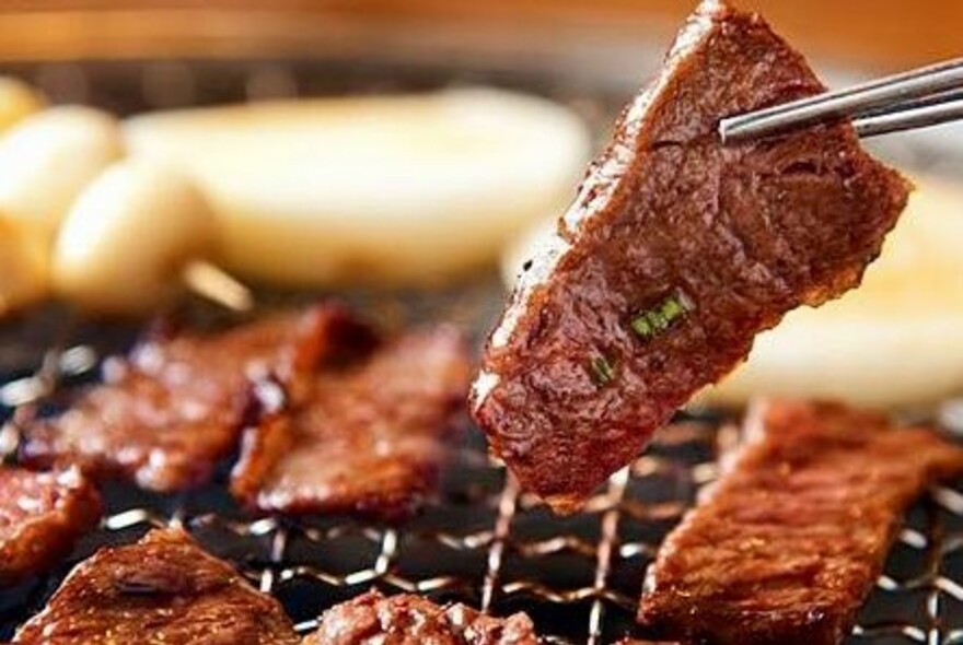 Metal chopsticks selecting pieces of meat from a grill.