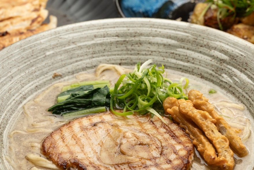 A bowl of Japanese pork ramen with sliced green vegetables as a garnish.