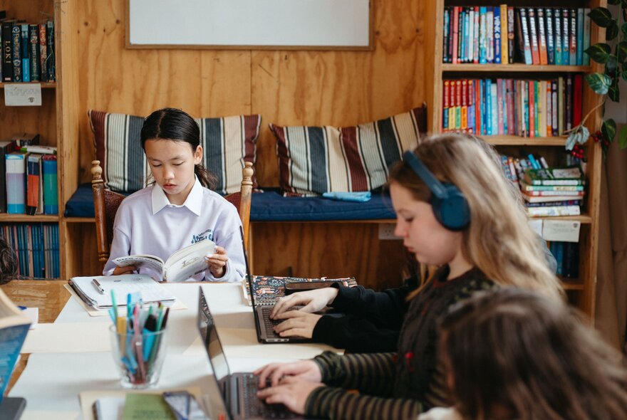 Kids in a classroom setting working at desks, one on a laptop with headphones. 