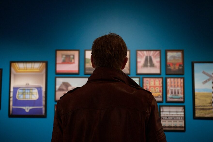 The dark back of a person looking at colourful artworks on a teal-blue wall.