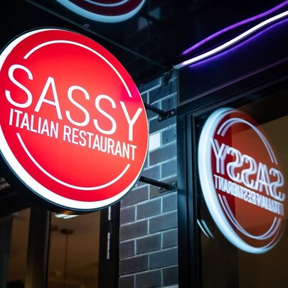 Sassy restaurant sign illuminated against brickwork.