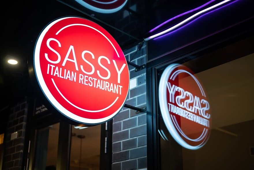 Sassy restaurant sign illuminated against brickwork.