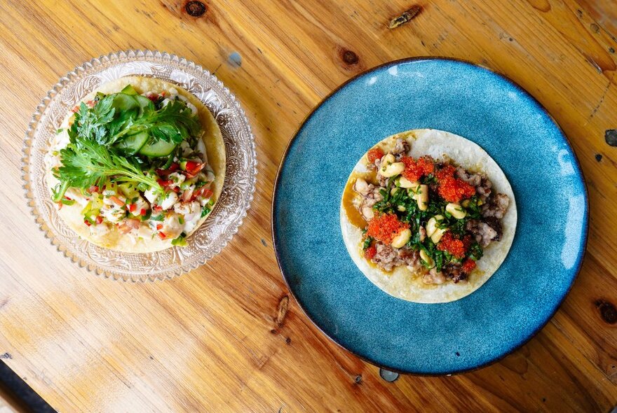 Looking down at two plates of food on a wooden table top.