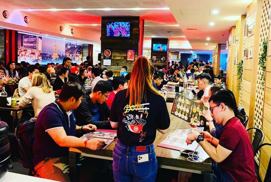 Interior of busy restaurant with patrons seated at tables and ordering from menus.