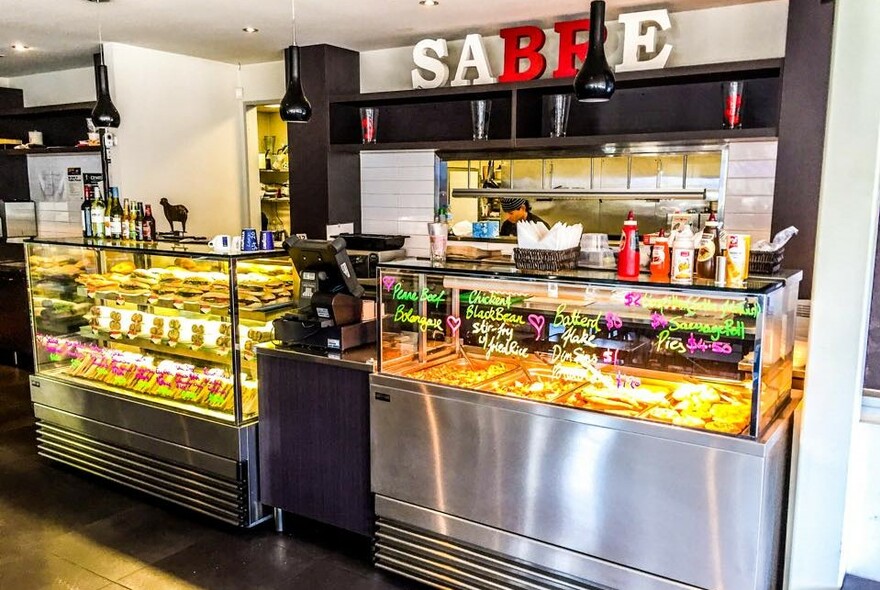 Cafe interior with signage above glass food counters and bain-marie with takeaway dishes.