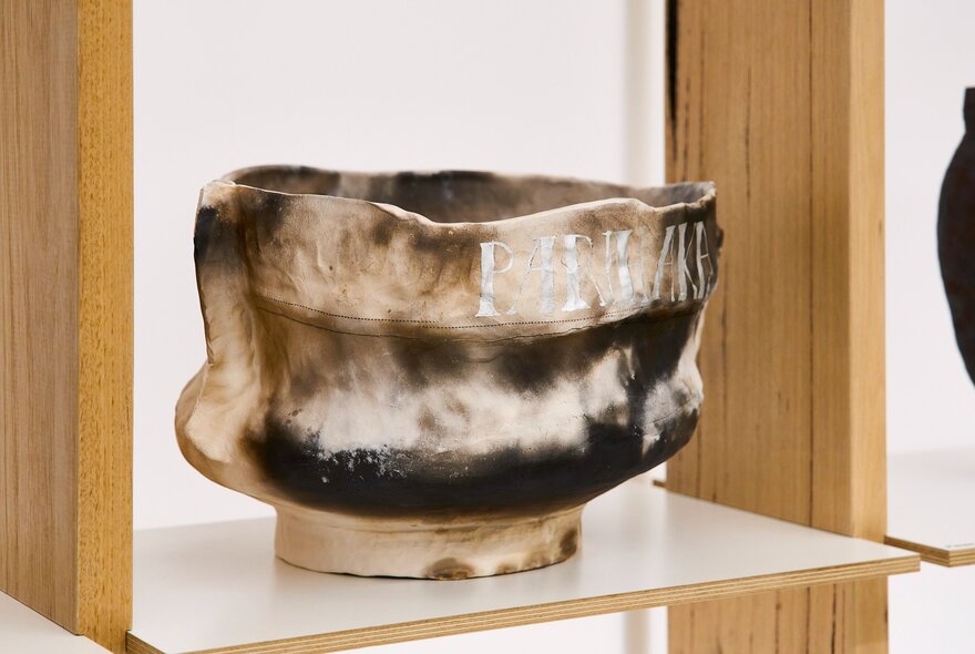 A brown and cream glazed ceramic piece on display on a shelf in a gallery.