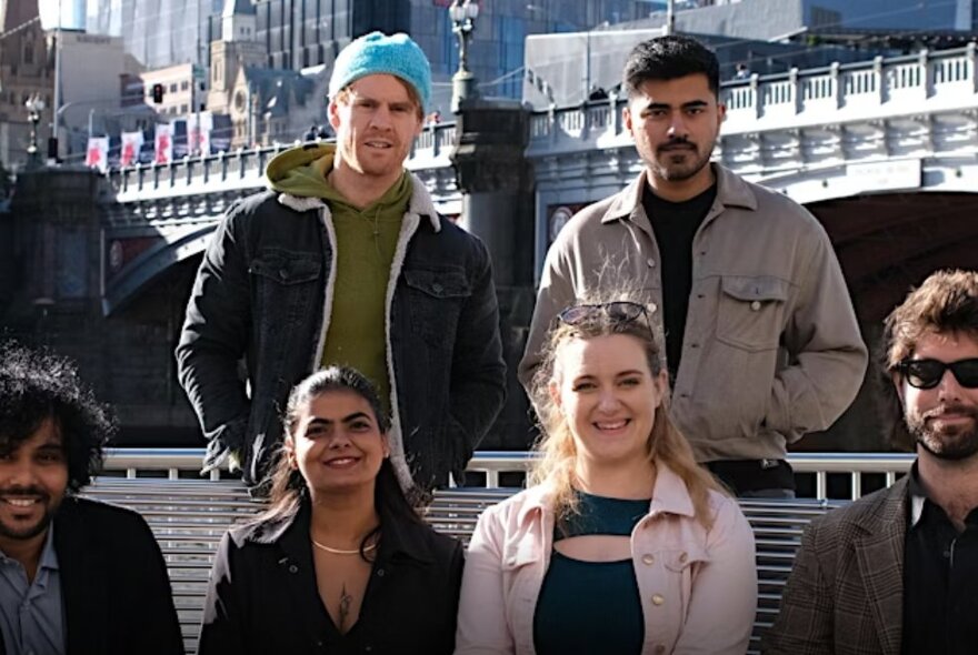 Group of six people seated and standing outside near Princes Bridge.