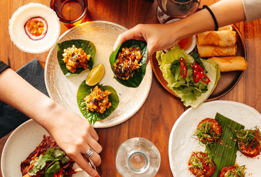 People reaching for Asian share dishes and cocktails in a restaurant.