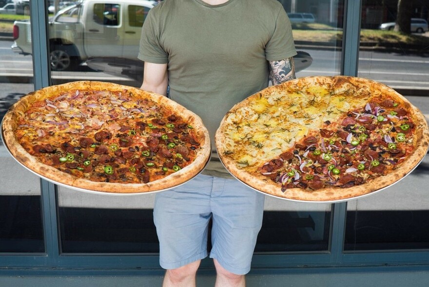 A person holding two very large half-and half pizzas.