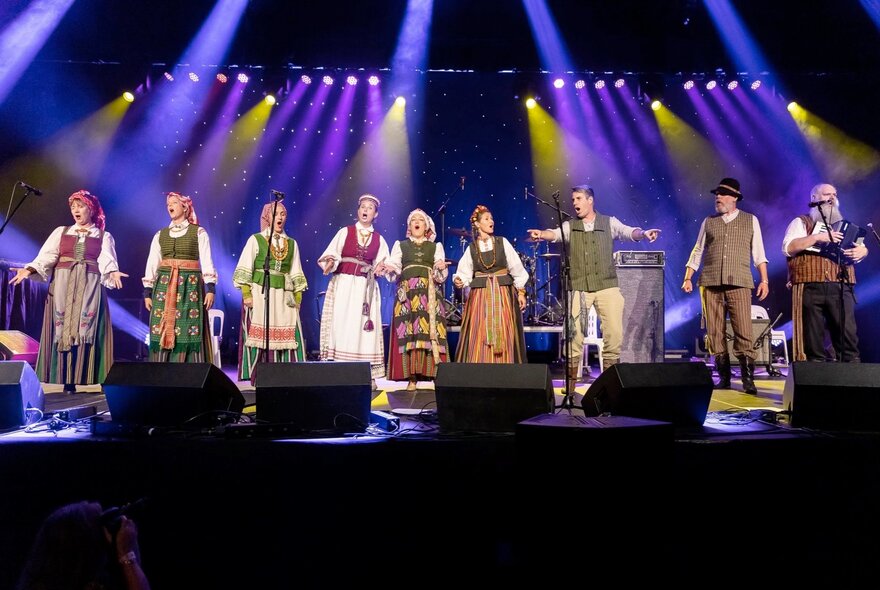 An ensemble of singers wearing traditional Lithuanian outfits singing on a stage.