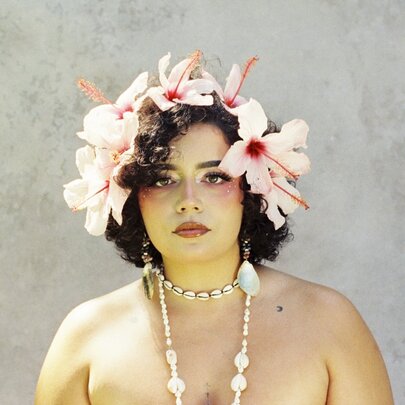 Australian artist Kee'ahn, posed wearing a floral headpiece and a shell necklace around her neck.
