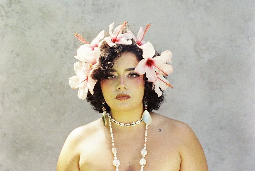 Australian artist Kee'ahn, posed wearing a floral headpiece and a shell necklace around her neck.