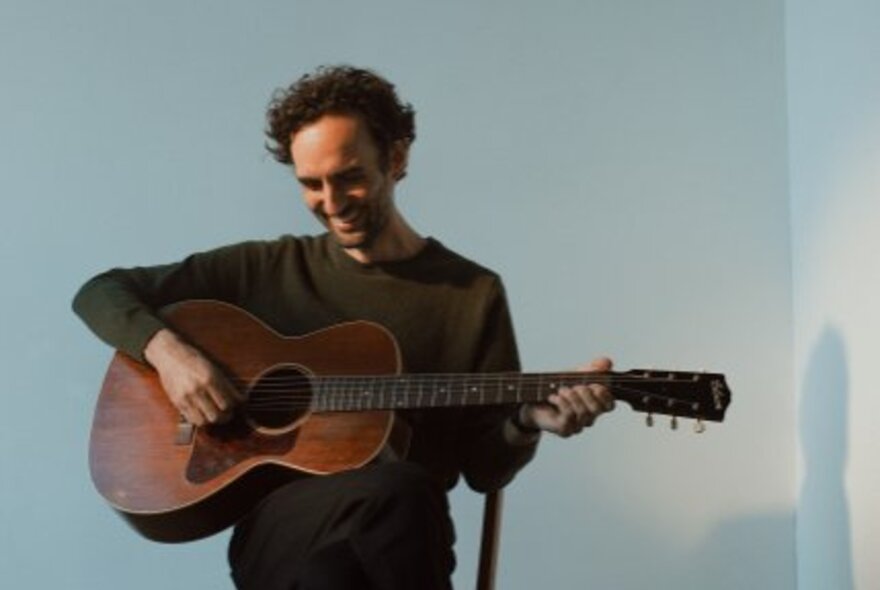 Guitar virtuoso and composer Julian Lage smiling and looking downwards while strumming his guitar. 