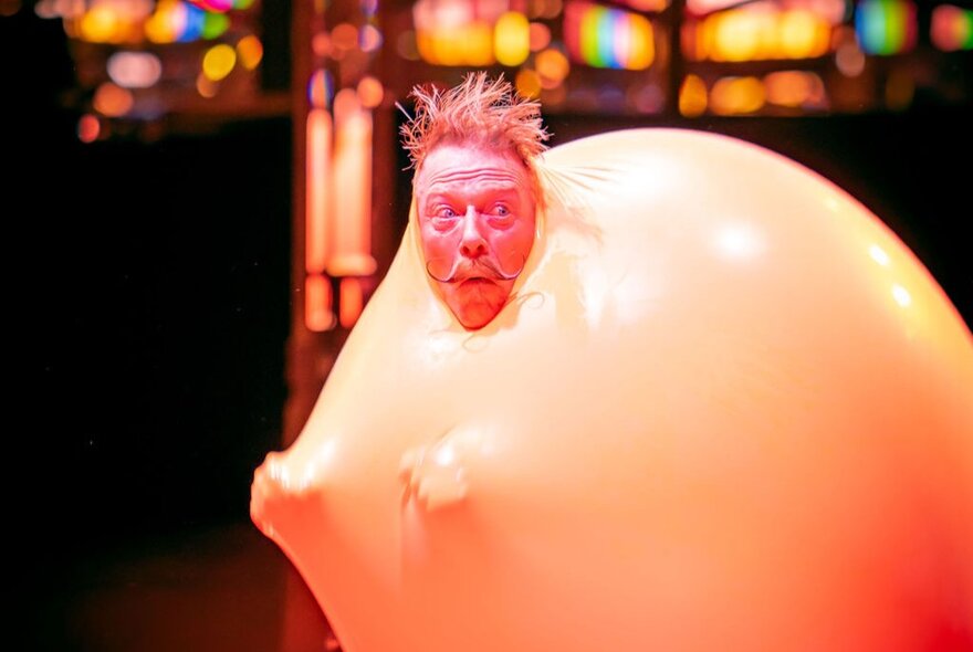 A man in a yellowish bubble suit with his head poking out and hands poking through from from within the suit. 