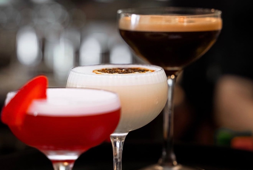Three different coloured cocktails, each in a wide champagne glass.