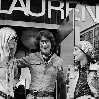 A black and white image of two models and a designer ourside of Yves St Laurent. 
