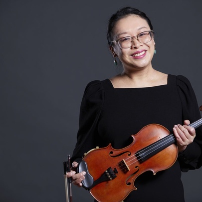 A woman smiling and holding a violin across her body.