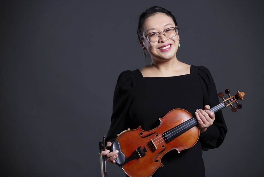 A woman smiling and holding a violin across her body.