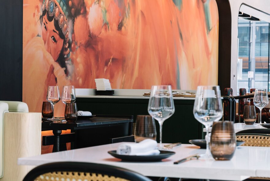 The interior of a restaurant showing a table with two place settings in front of a peach-coloured wall mural.