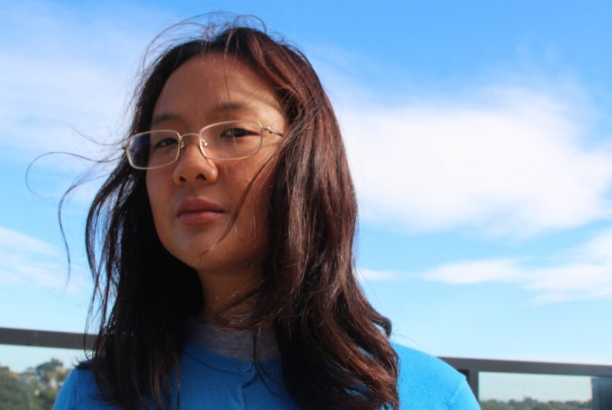 A woman looking serious, blue sky with wispy clouds behind her. 