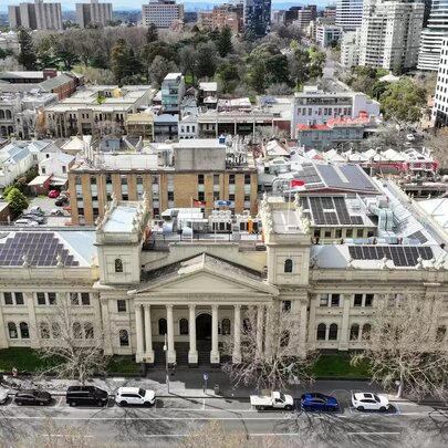 An aerial, wide shot of Trades Hall Melbourne, a large, historical, light-coloured stone building with neoclassical architecture featuring a prominent central portico with columns.