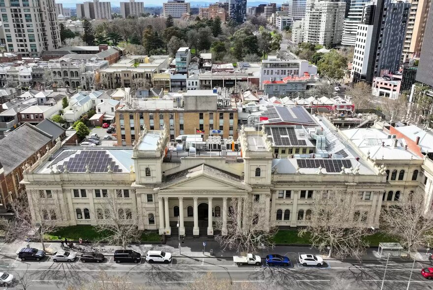 An aerial, wide shot of Trades Hall Melbourne, a large, historical, light-coloured stone building with neoclassical architecture featuring a prominent central portico with columns.