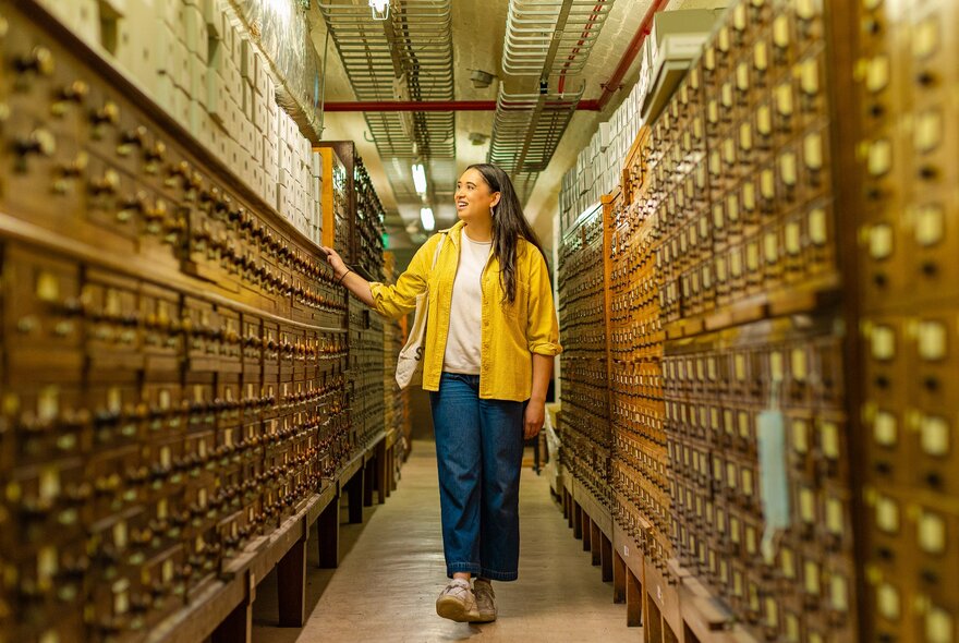 A woman is walking through a corridor filled with old library catalogues.