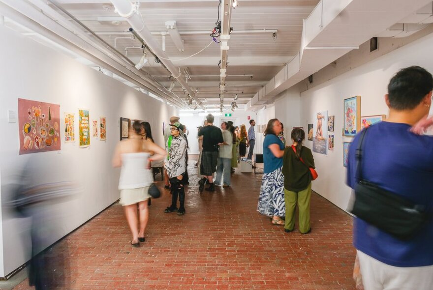 Groups of people looking at art in a long, narrow gallery space.
