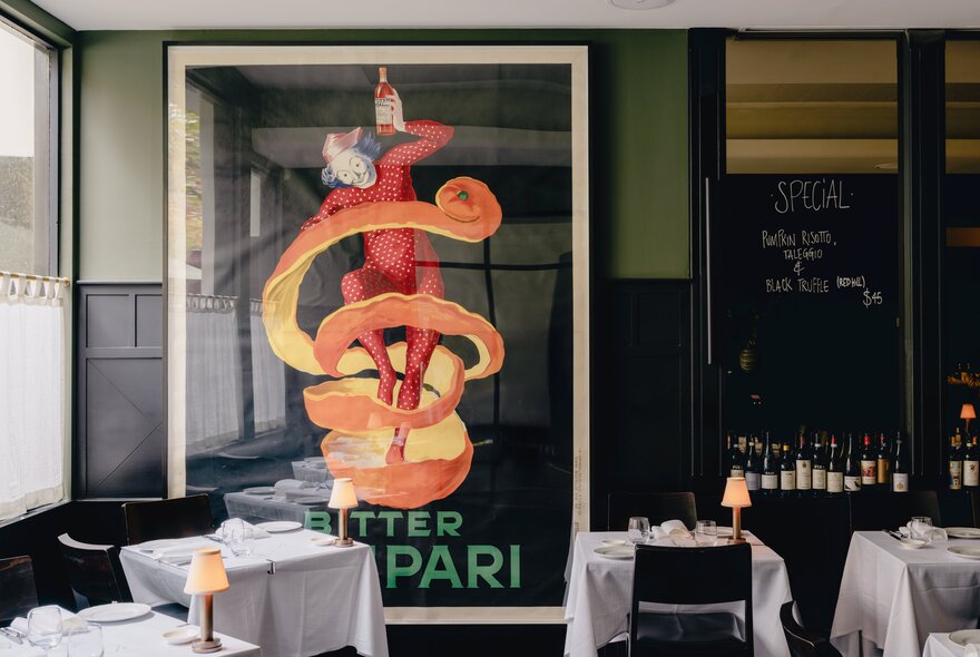The dining room interior of Cafe Florentino restaurant on Bourke Street with a billboard-size Campari poster on the wall, tables covered in white linen and dark dining chairs.