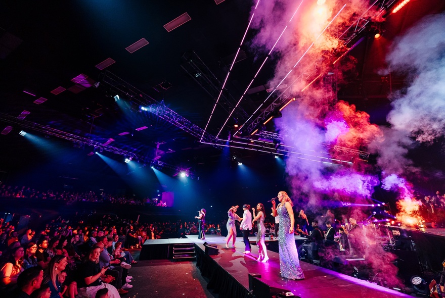 Singers on stage performing a show on the stage at Festival Hall to a seated audience.