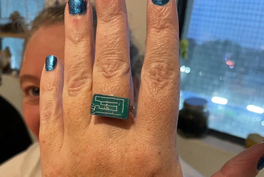 A hand modelling a green ring that has been carved from soapstone.