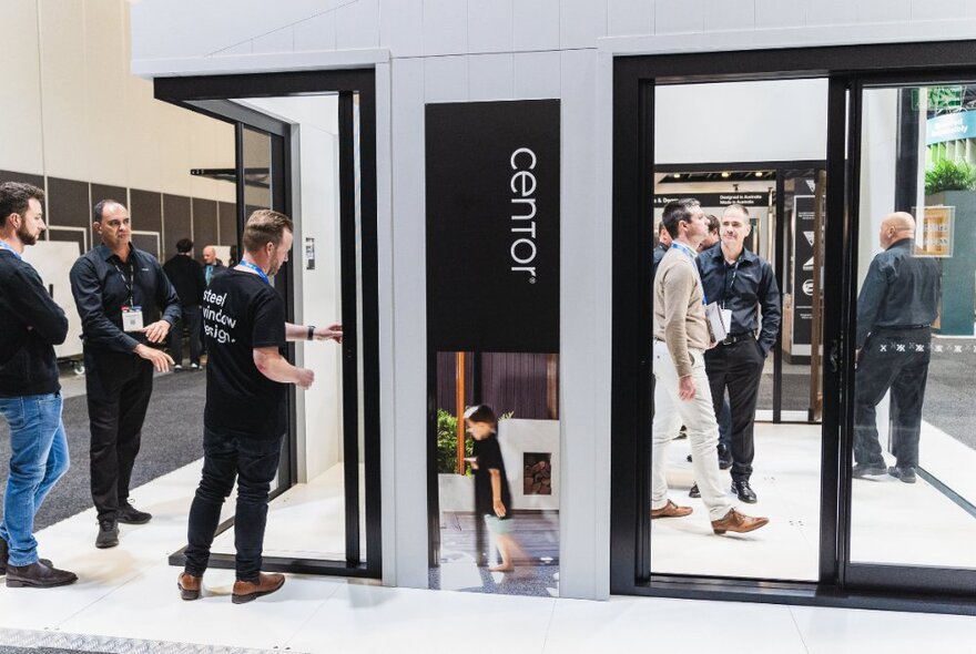 People at a design expo exploring a stall with black-framed windows.