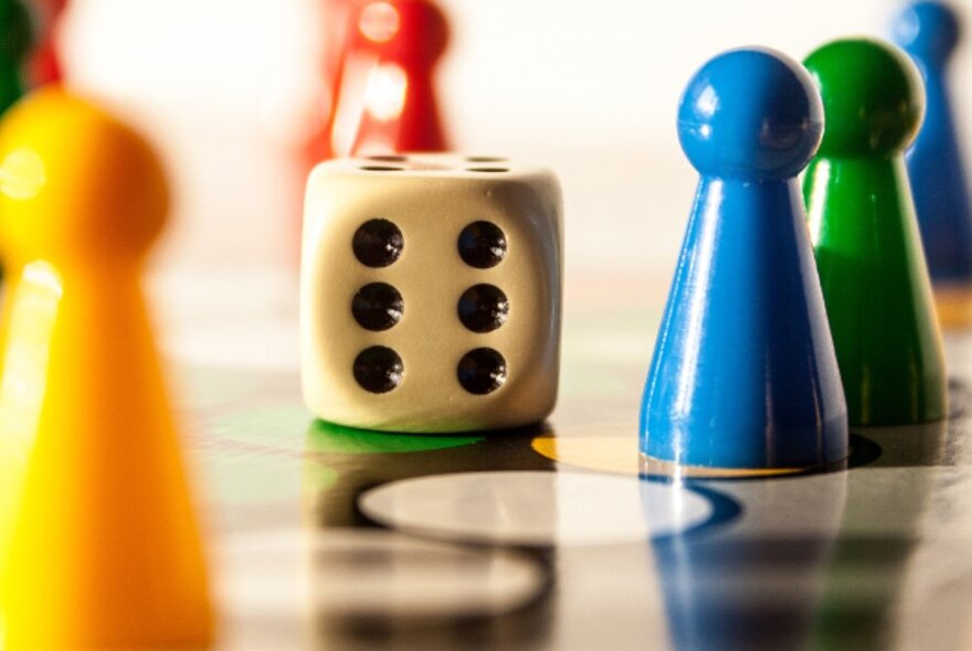 A close up of a single dice on a shiny board, surrounded by coloured upright 3D tokens that move around the board.