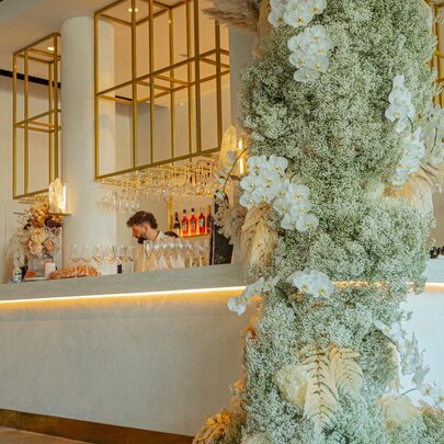 A cafe bar festooned with grey-green foliage and white blooms, staff behind the counter. 