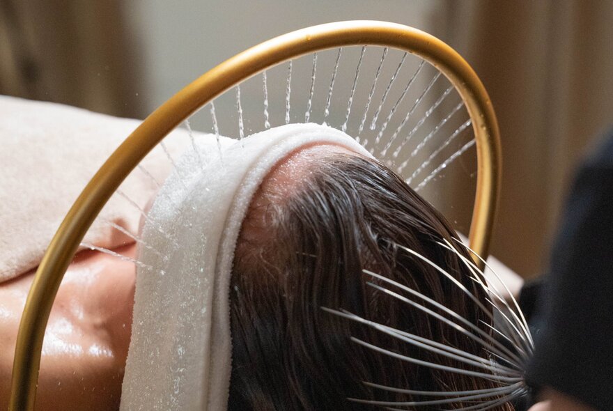 A woman receiving a speclised spa treatment with a white cloth over her eyes and a bronze ring providing a water massage.