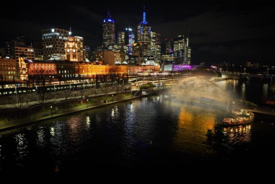 The city skyline at night with a cloud of fog around a bridge.