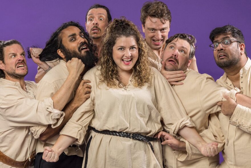 A group of actors dressed in beige clowning around for a group photo. 