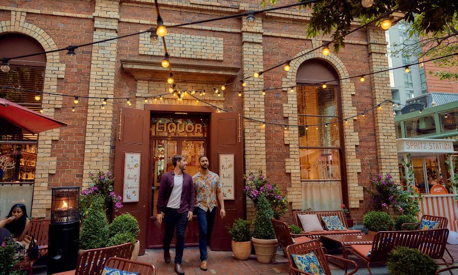 Two men walking through a restaurant's outdoor dining area under festoon lighting.