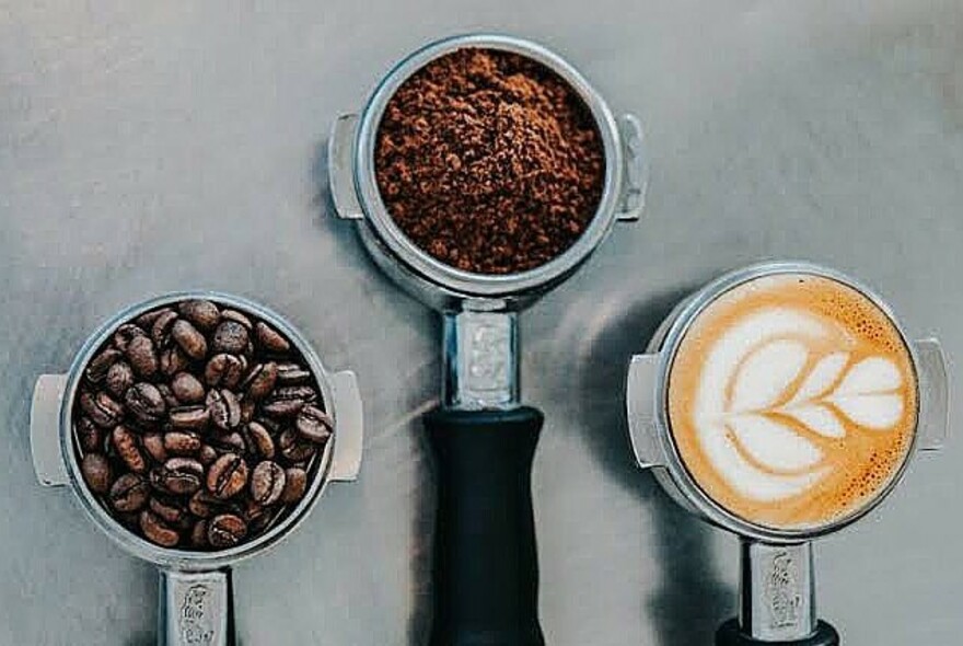 Three coffee portafilters filled with coffee beans, ground coffee and decorated coffee foam.